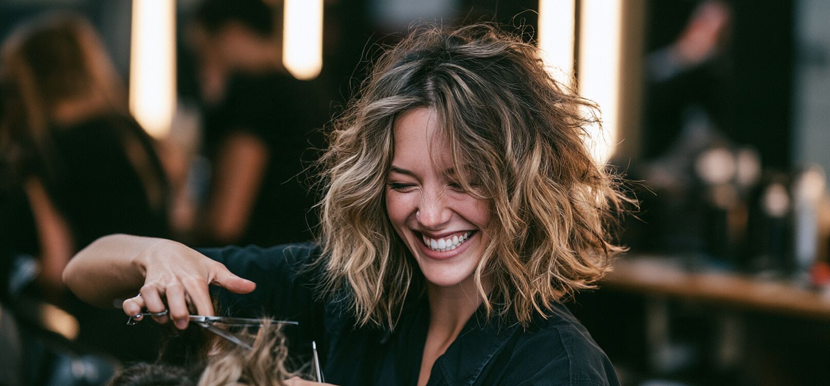 Hairstylist laughing while cutting a client&rsquo;s hair in a salon